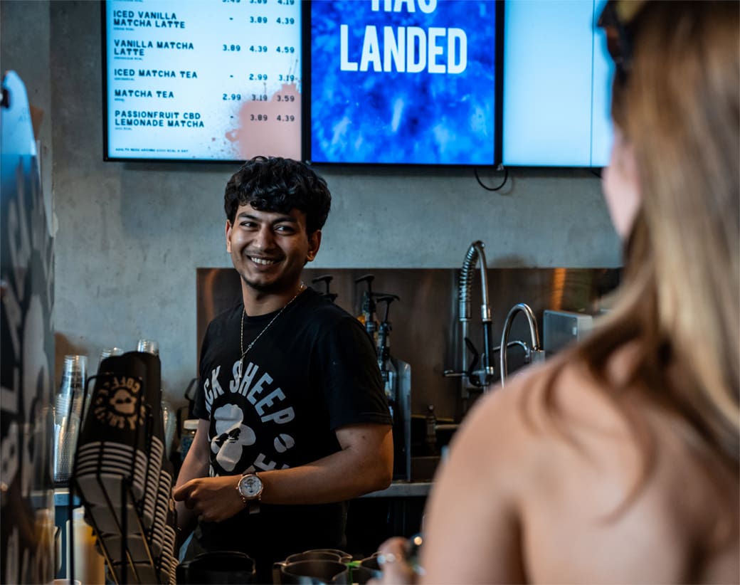 Counter worker in a coffee shop smiling and serving a customer